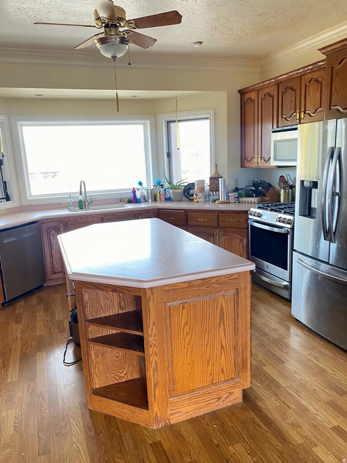 Kitchen featuring stainless steel appliances, open shelves, light countertops, a textured ceiling, and ornamental molding
