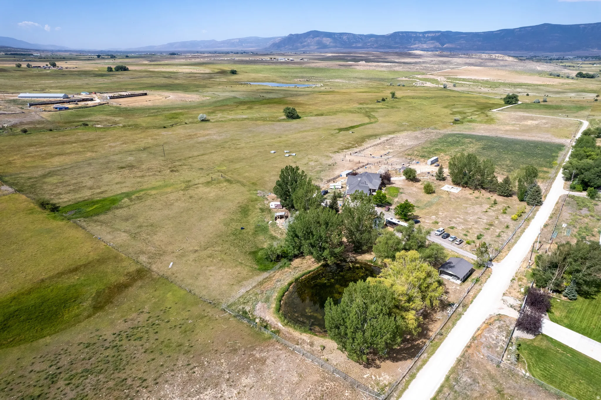 Expansive property featuring a private pond, established trees, a main residence with a dark roof, a detached structure, and a gravel driveway