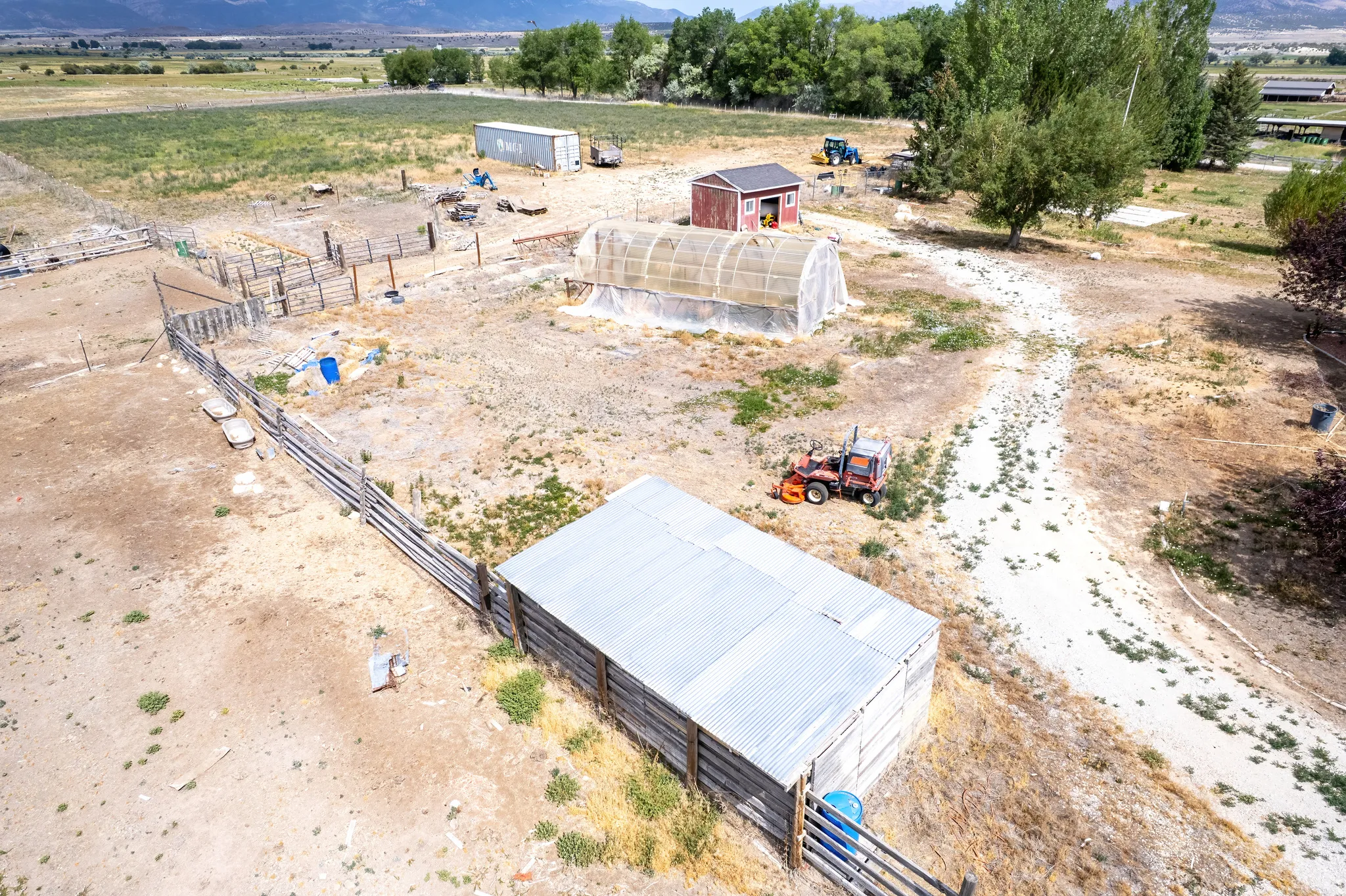 Expansive agricultural property featuring multiple outbuildings, including a red shed, a large hoop house, and a long barn with a metal roof