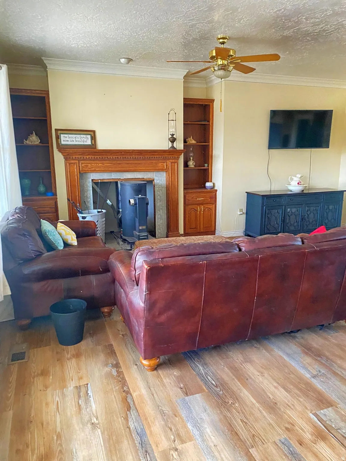 Living room with built in shelves, a textured ceiling, ornamental molding, wood-type flooring, and ceiling fan