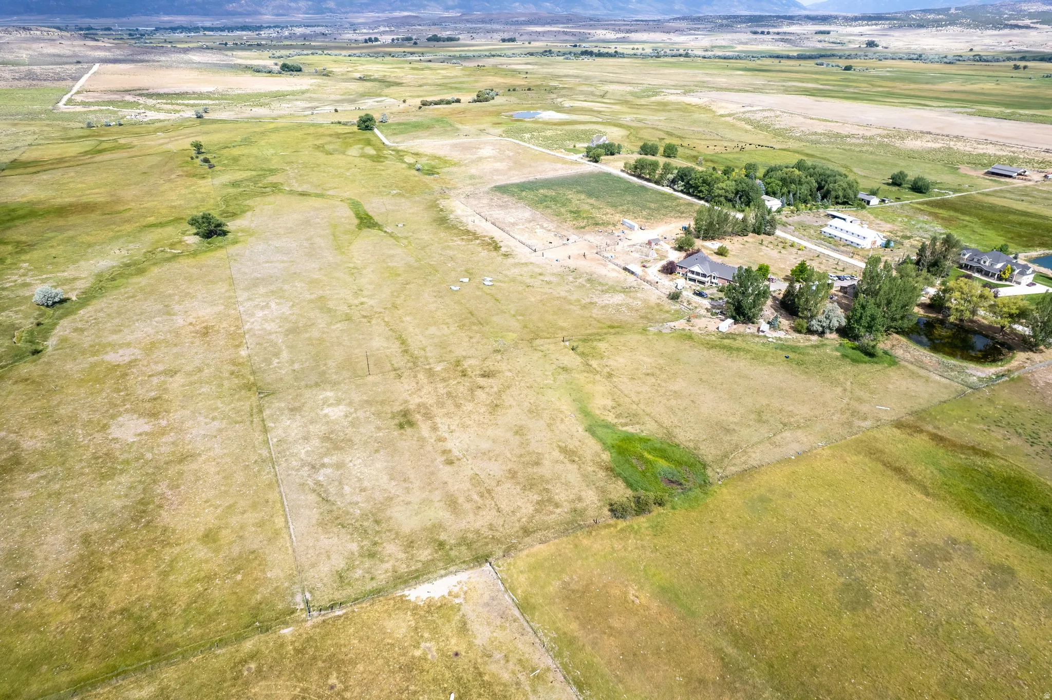 Expansive rural property featuring multiple structures, open fields, mature trees, and visible water features