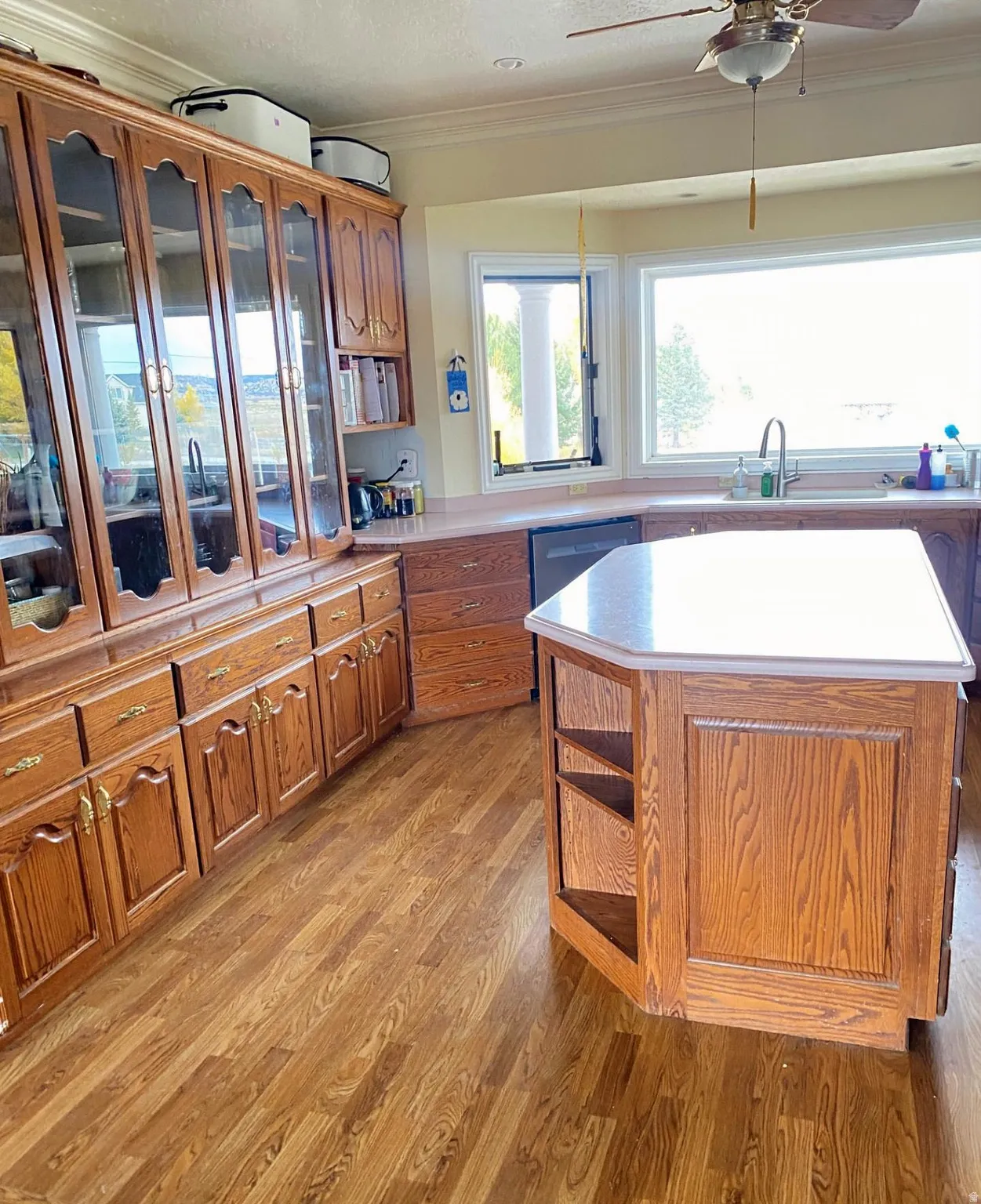 Kitchen with crown molding, brown cabinets, light countertops, light wood-style flooring, and glass insert cabinets