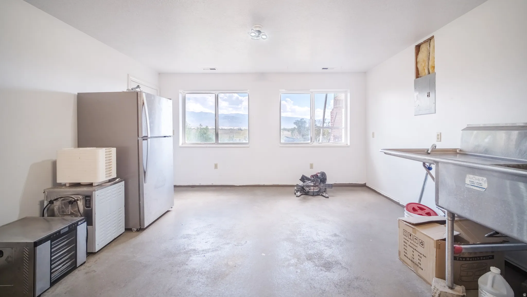 Spacious utility room featuring two large windows, a stainless steel commercial sink, and a durable concrete floor