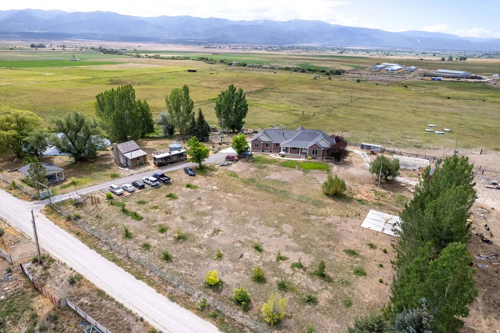 Expansive property featuring a single-story residence with a covered front porch, multiple outbuildings, and a surrounding natural landscape