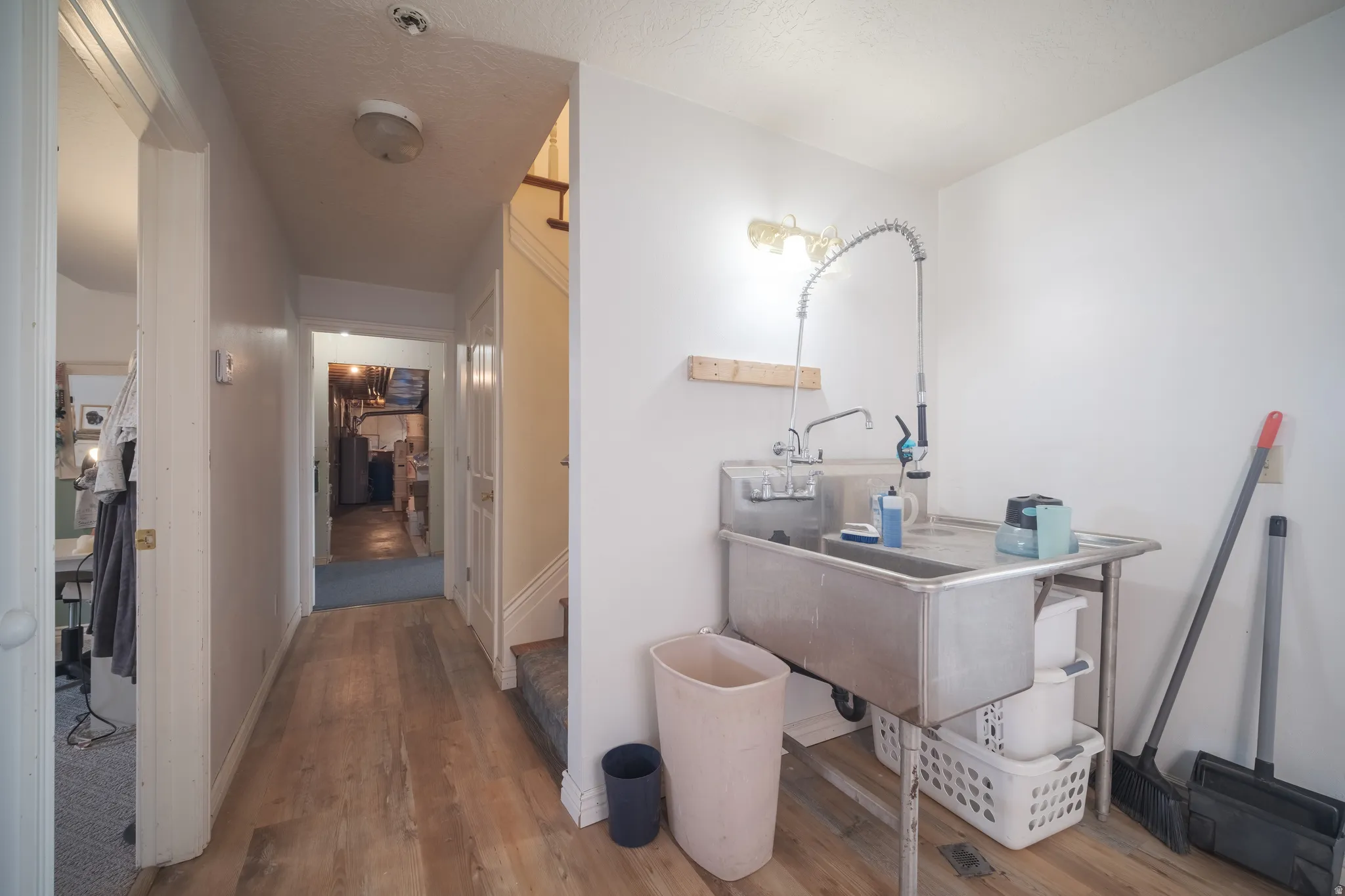 Utility area featuring a stainless steel sink with a professional-style faucet, wood-finish flooring, and white painted walls