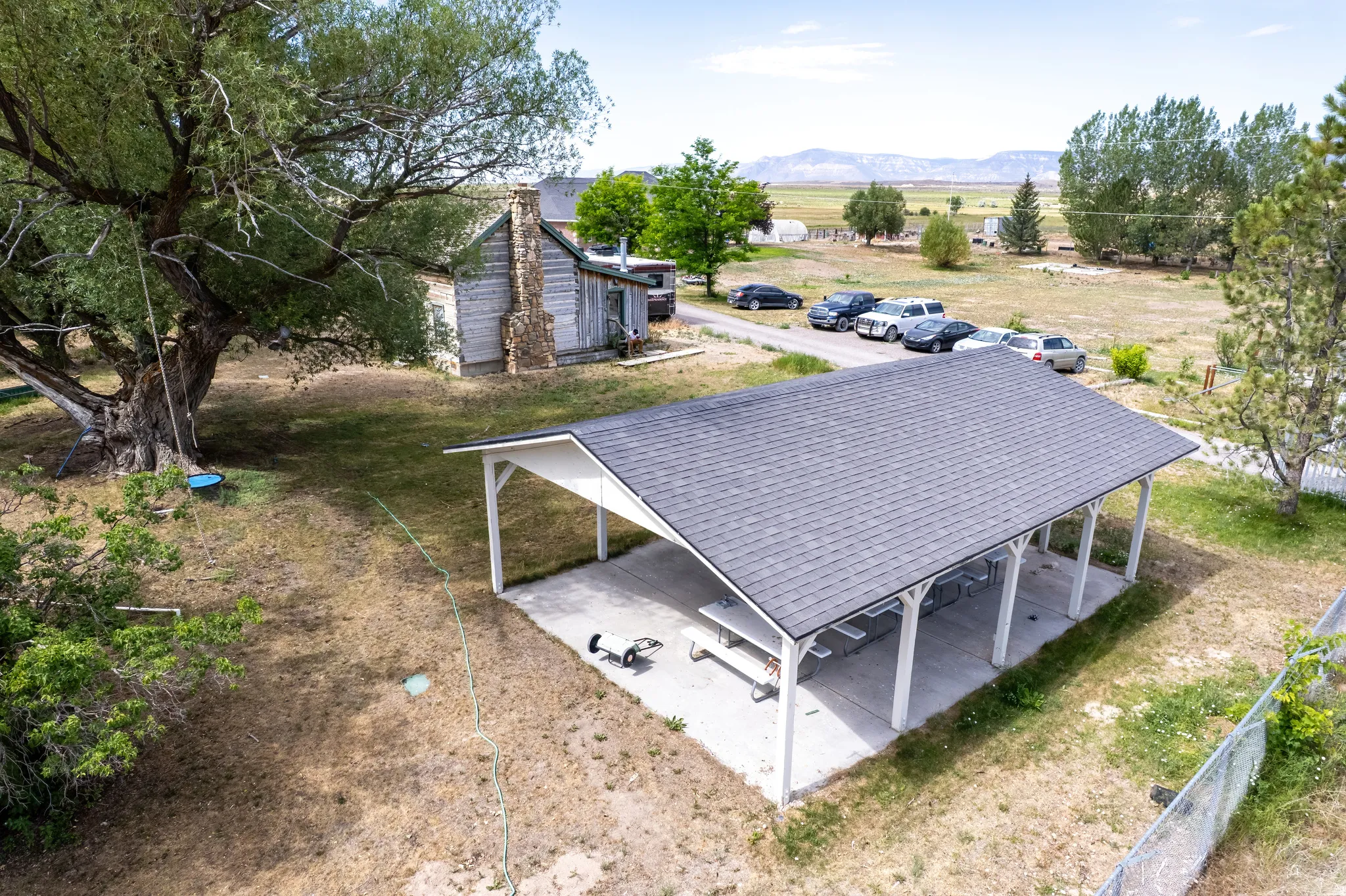 Spacious outdoor pavilion with a dark shingle roof and white support columns, situated on a concrete slab