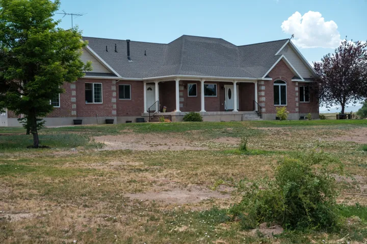 Expansive brick-faced ranch-style residence featuring a covered front porch with white columns, multiple gabled rooflines, and an arched window