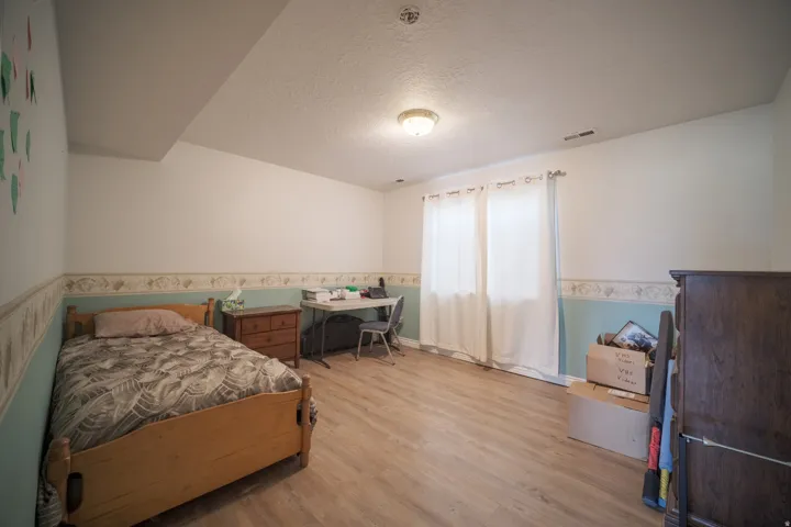 Room with light wood-finish flooring, two windows with white curtains, white and blue painted walls with a decorative border, and a ceiling-mounted light fixture