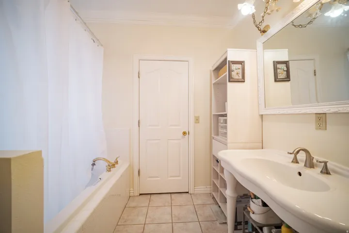 Bathroom featuring a ceramic tile floor, white built-in bathtub with brass fixtures, pedestal sink with brushed nickel faucet, large framed wall mirror, and integrated shelving unit