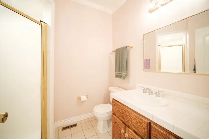 Bathroom with a wood-finish vanity, white tile countertop, and an integrated sink with a chrome faucet
