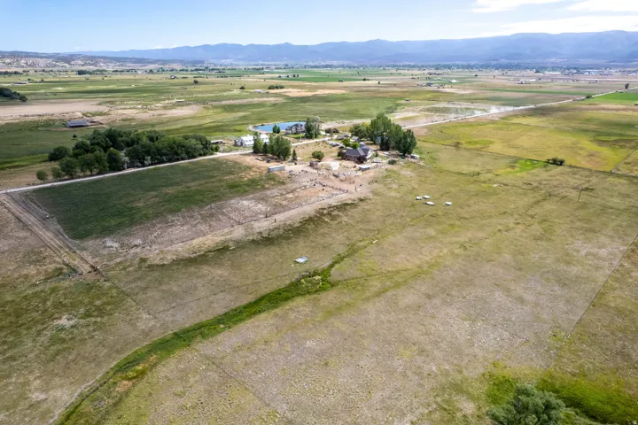 Expansive agricultural land featuring a central residential cluster, a pond, and distant mountain ranges