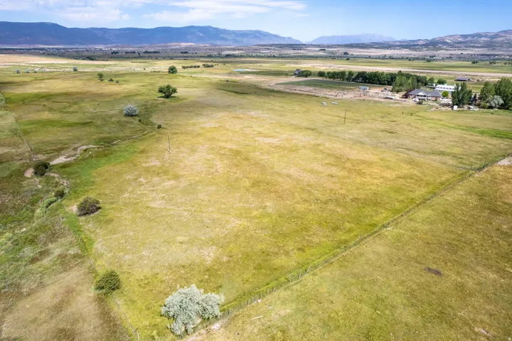 Expansive rural acreage featuring green and golden fields, distant mountain ranges, scattered trees, and a distant property with structures