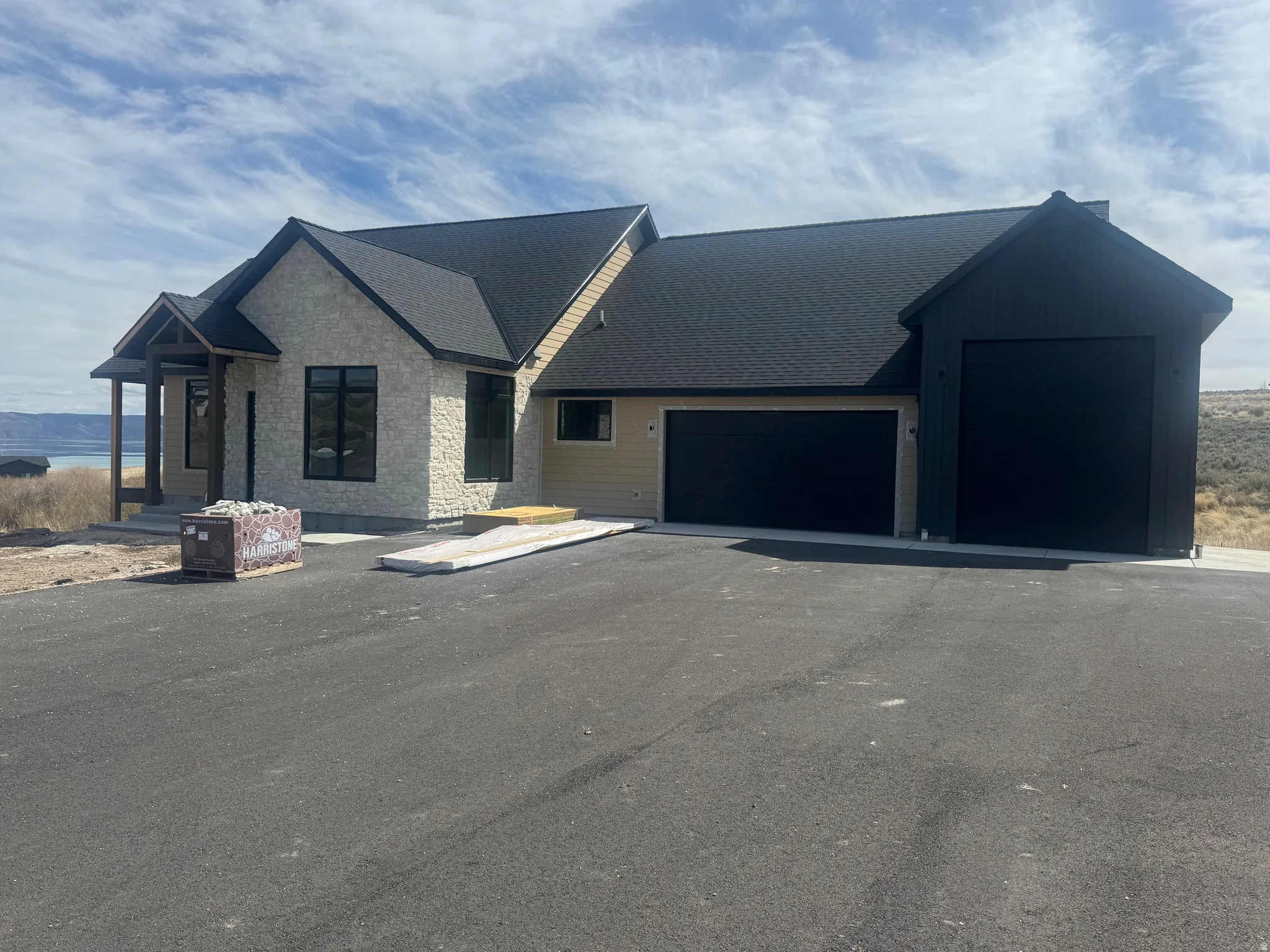 Modern farmhouse with stone siding, an attached garage, asphalt driveway, and roof with shingles