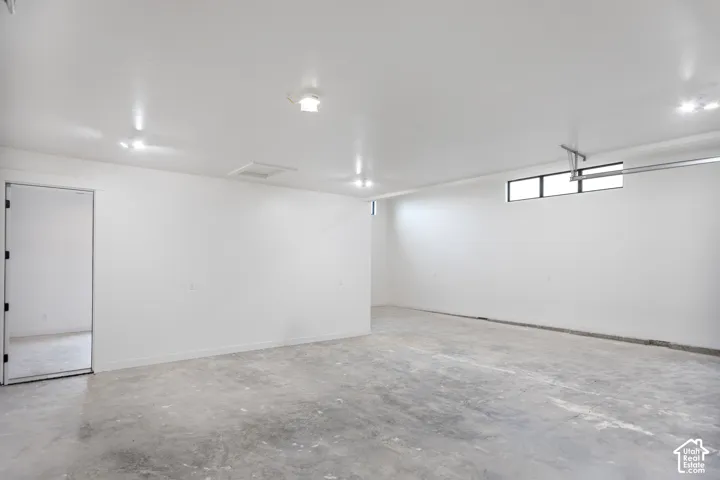 Concrete flooring, white painted walls, track lighting, an overhead door mechanism, and a rectangular window