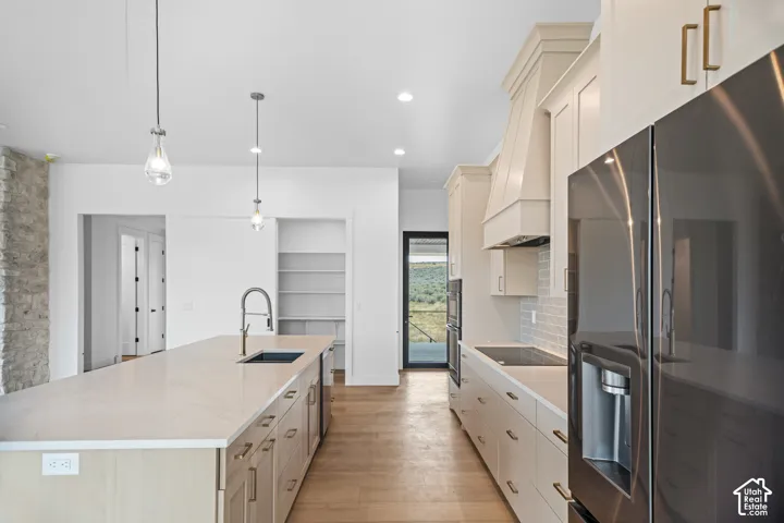 Spacious kitchen featuring a large island with an undermount sink, pendant lighting, stainless steel appliances, and wood-finish flooring