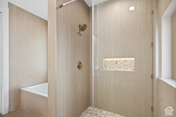 Glass-enclosed shower with a river rock floor, illuminated shower niche, and brushed brass fixtures