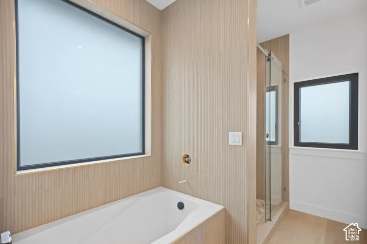 Built-in tub with gold-finish fixtures, textured wall tile surround, large frosted privacy window, and glass-enclosed shower