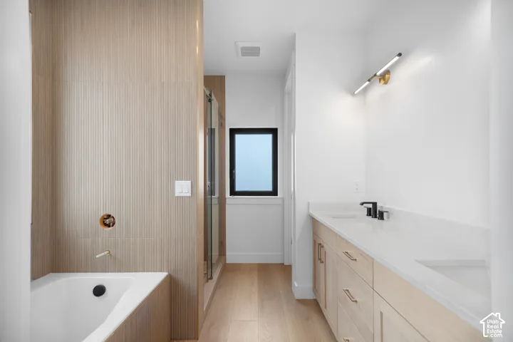 Light wood-finish flooring, a built-in bathtub, and a double vanity with stone countertops