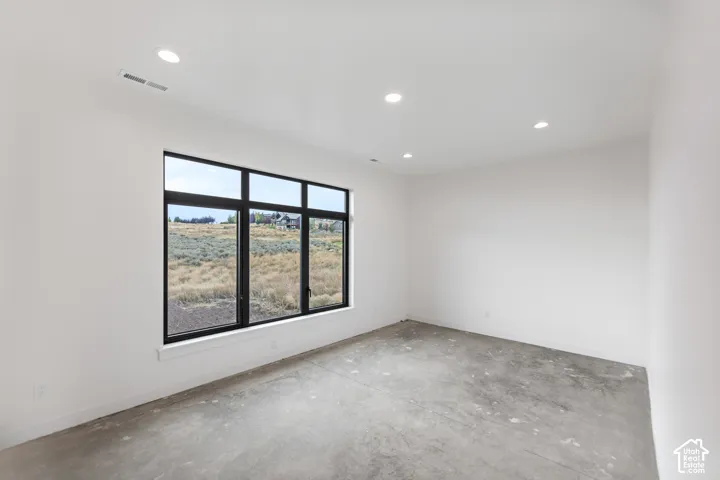 Expansive room featuring a large black-framed window, recessed ceiling lights, and concrete flooring