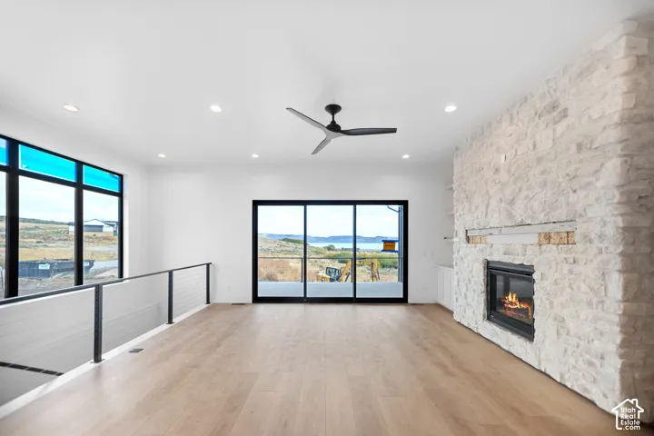 Spacious room with wood-finish flooring, a stone-clad fireplace with a hearth, a black ceiling fan, and large windows