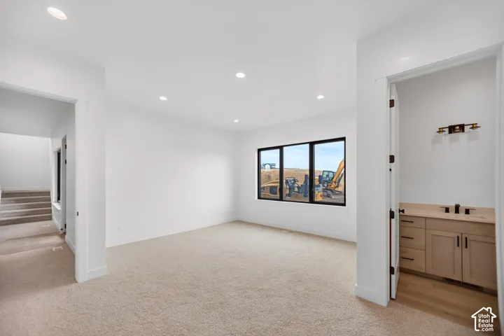 Recessed ceiling lighting, wall-to-wall carpeting, multiple windows with black frames, built-in vanity with cabinetry, and light-toned flooring