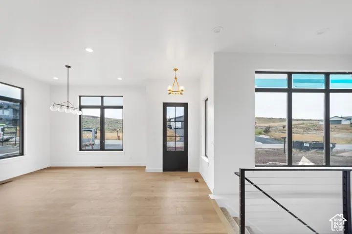 Wood-finish flooring, multiple large windows with black framing, high ceilings with recessed lighting, black framed entry door with glass panels, and a modern stair railing with cable infill