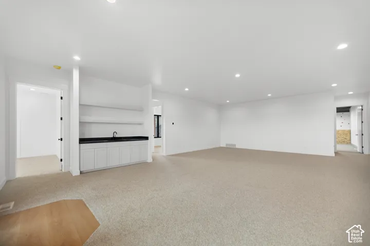 Spacious open area featuring recessed lighting, light-toned carpeting, and a built-in wet bar with white cabinetry and a dark countertop