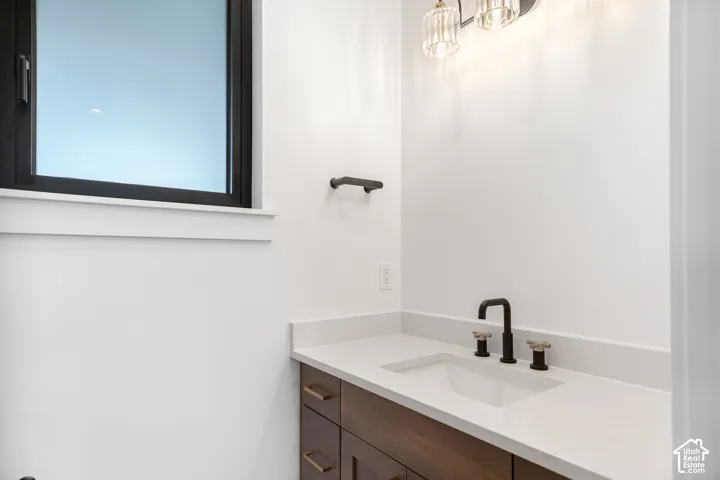 Floating wood-finish vanity with an integrated sink, light-toned countertop, matte black faucet, and contemporary light fixture