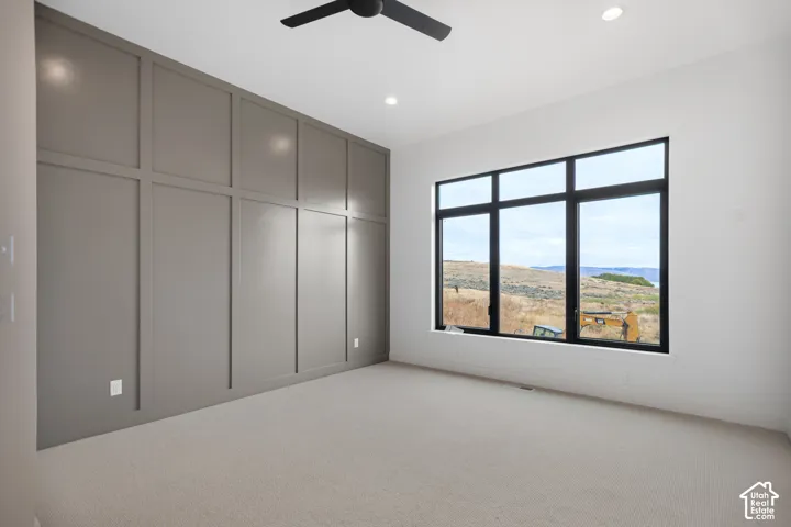 Accent wall with panel molding, large multi-pane window, flush-mounted ceiling lighting, and a ceiling fan