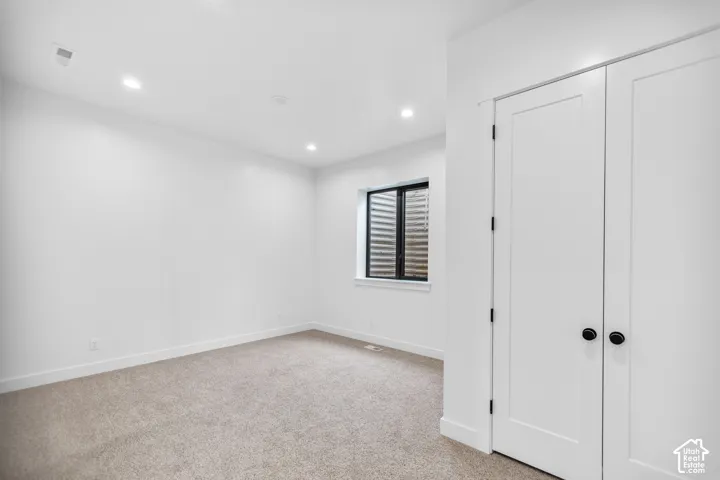 Recessed lighting, neutral-tone carpeting, window with black trim, and white bi-fold doors with matte black hardware