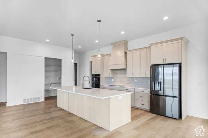 Kitchen featuring wood-finish flooring, a large island with a sink, pendant lighting, recessed lighting, and a barn door pantry