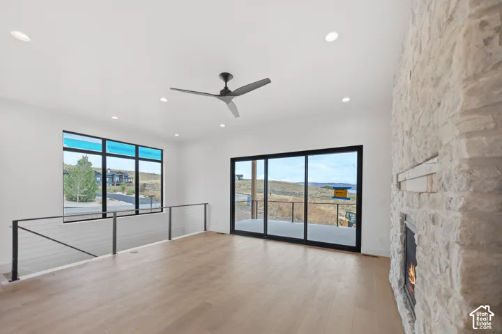 Spacious room with wood-finish flooring, a stone-clad fireplace, large sliding glass doors, a prominent window, and recessed lighting