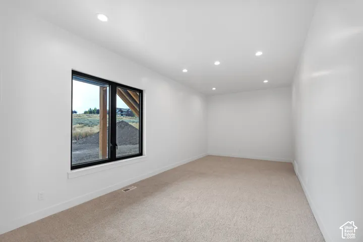 Recessed lighting illuminates this room featuring light-toned carpeting and a large window with black trim