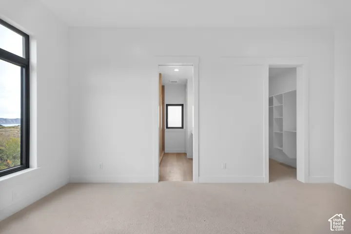 Large window with black frame, neutral wall paint, carpet flooring, built-in shelving, and wood-finish flooring in the adjoining space