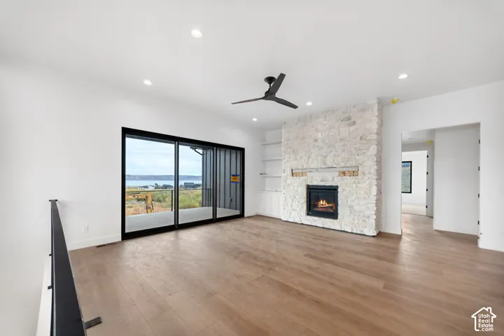 Wood-finish flooring, stone-clad fireplace, integrated shelving, black ceiling fan, and recessed lighting