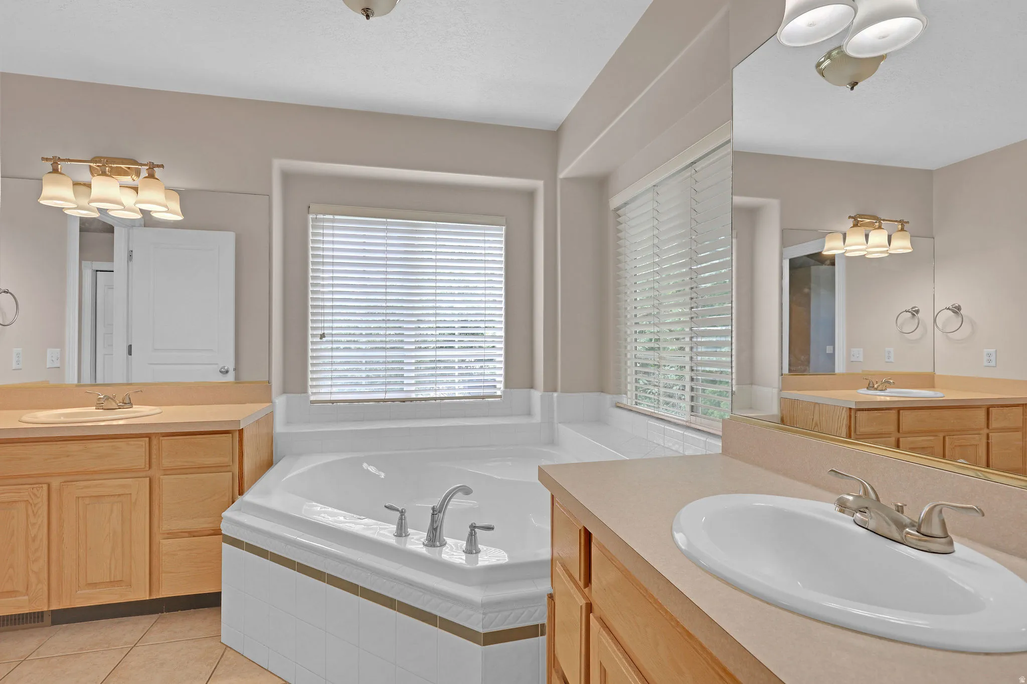 Bathroom featuring two vanities, a garden tub, and light tile patterned floors