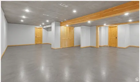 Expansive unfinished space featuring concrete flooring, exposed wood beams, recessed lighting, neutral painted walls, and natural wood doors