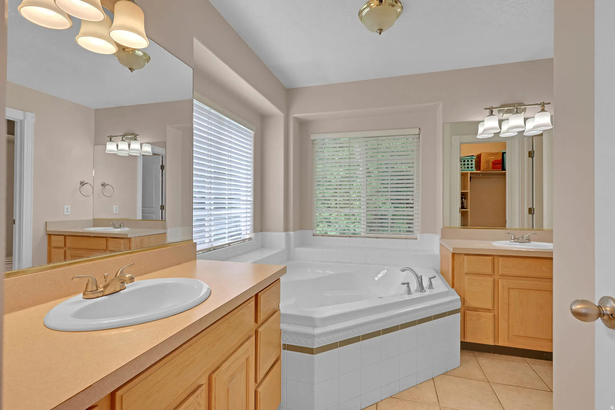 Bathroom featuring light tile patterned floors, a garden tub, and two vanities