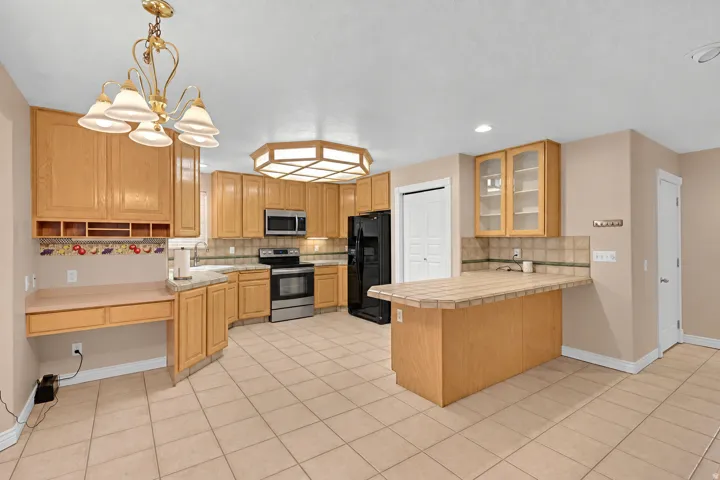 Kitchen featuring tile flooring, light wood cabinetry, a built-in desk area, and stainless steel appliances. (Digitally altered with replaced appliances)