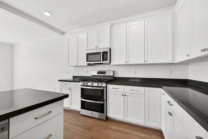 Kitchen with appliances with stainless steel finishes, light wood-style flooring, white cabinets, beam ceiling, and a textured ceiling