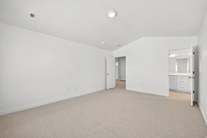 Unfurnished bedroom with vaulted ceiling, light carpet, and ensuite bathroom