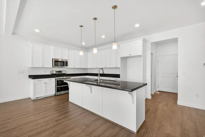 Kitchen with a kitchen breakfast bar, white cabinetry, stainless steel appliances, a center island with sink, and recessed lighting