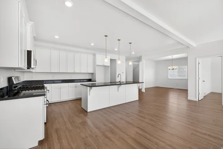 Kitchen featuring a breakfast bar, a center island with sink, gas stove, pendant lighting, and white cabinets