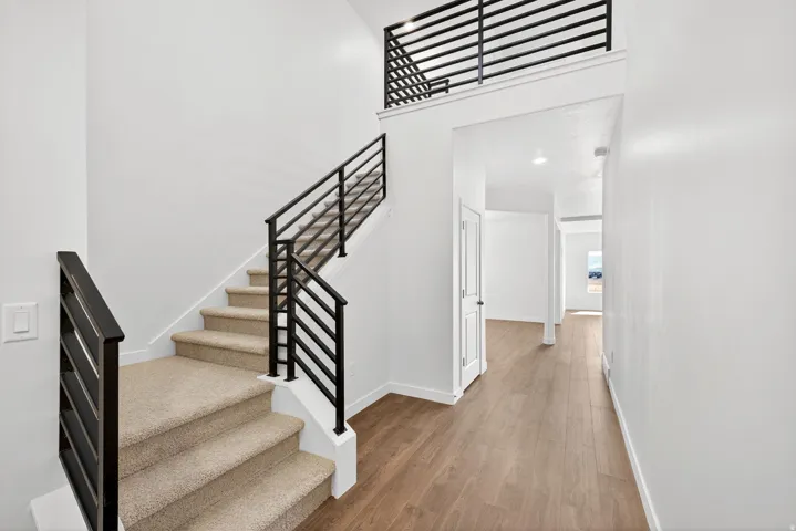 Stairs with a towering ceiling, wood finished floors, and recessed lighting