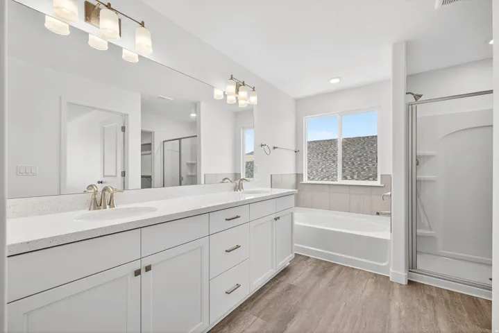 Full bath featuring a shower stall, double vanity, a garden tub, and light wood-style flooring