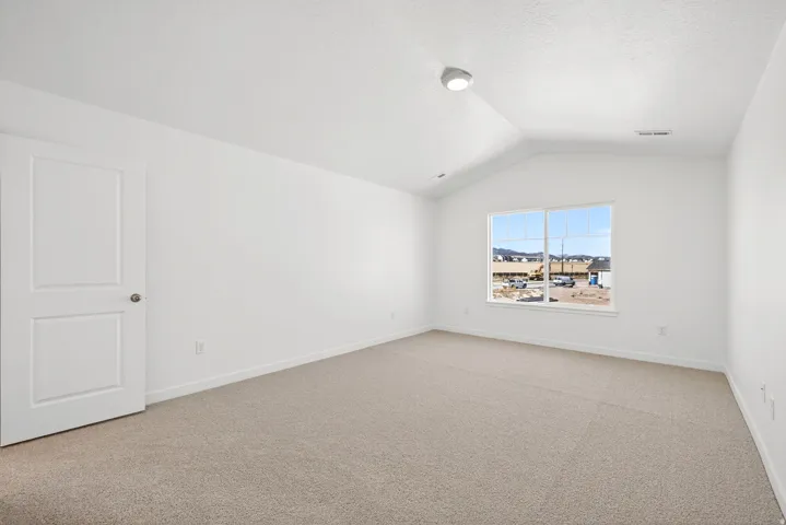 Unfurnished room with light carpet, vaulted ceiling, and a textured ceiling