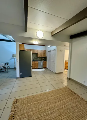 Kitchen featuring beamed ceiling, light tile patterned floors, stainless steel appliances, brown cabinetry, and a textured ceiling