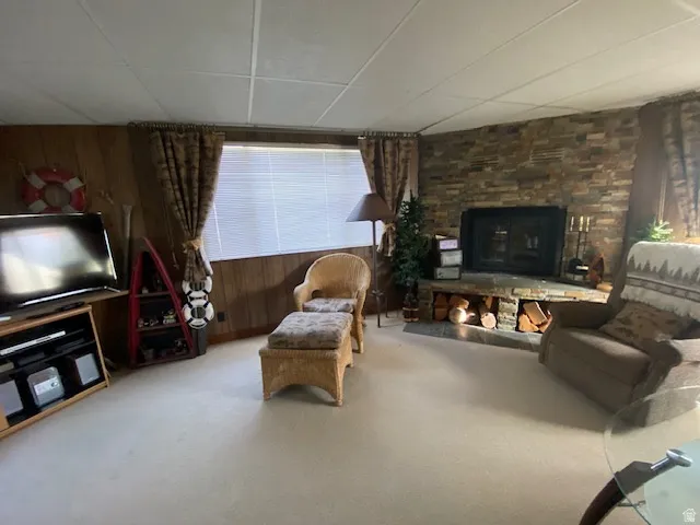 Carpeted living room featuring wooden walls, a stone fireplace, and a drop ceiling