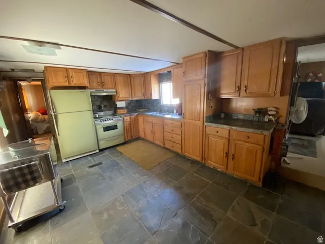 Kitchen featuring freestanding refrigerator, range, stone tile floors, brown cabinetry, and double oven