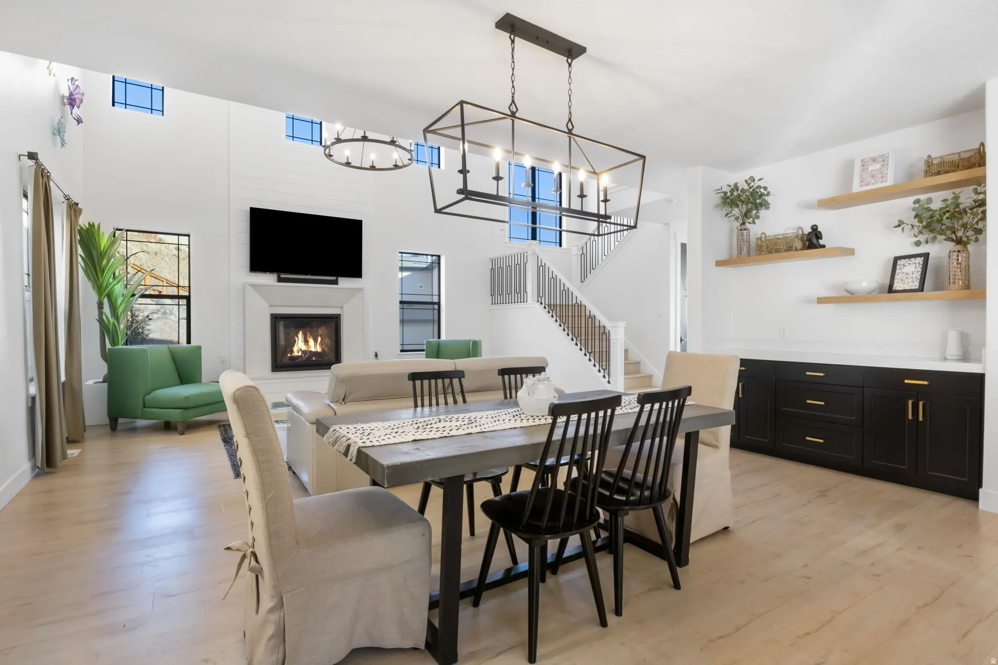 Dining room featuring a glass covered fireplace, light wood-style floors, stairs, a high ceiling, and a chandelier